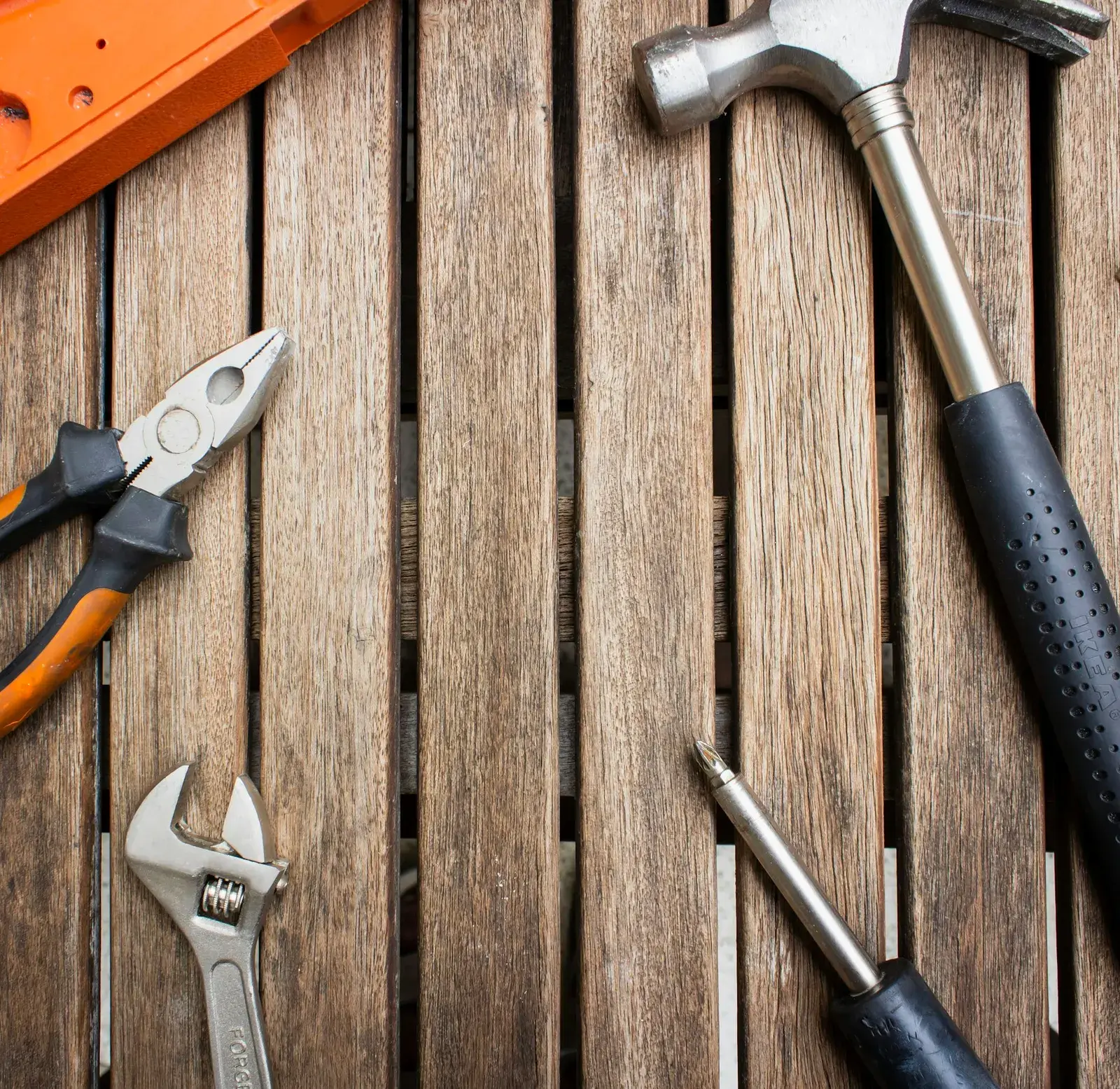 Pliers, a wrench and a screwdriver arranged on a wooden table.
