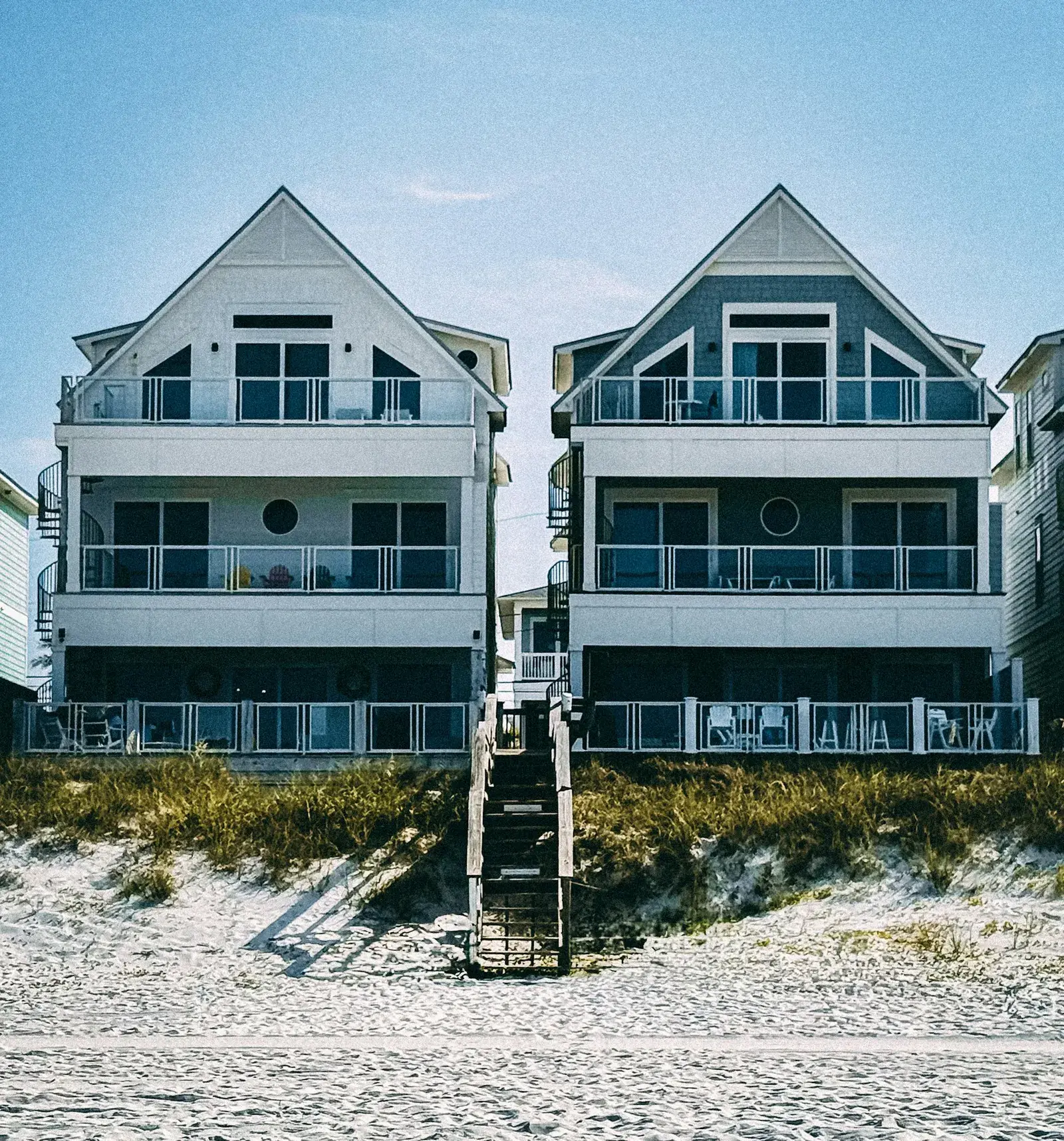 Two modern beach houses with stairs leading down to the sand.