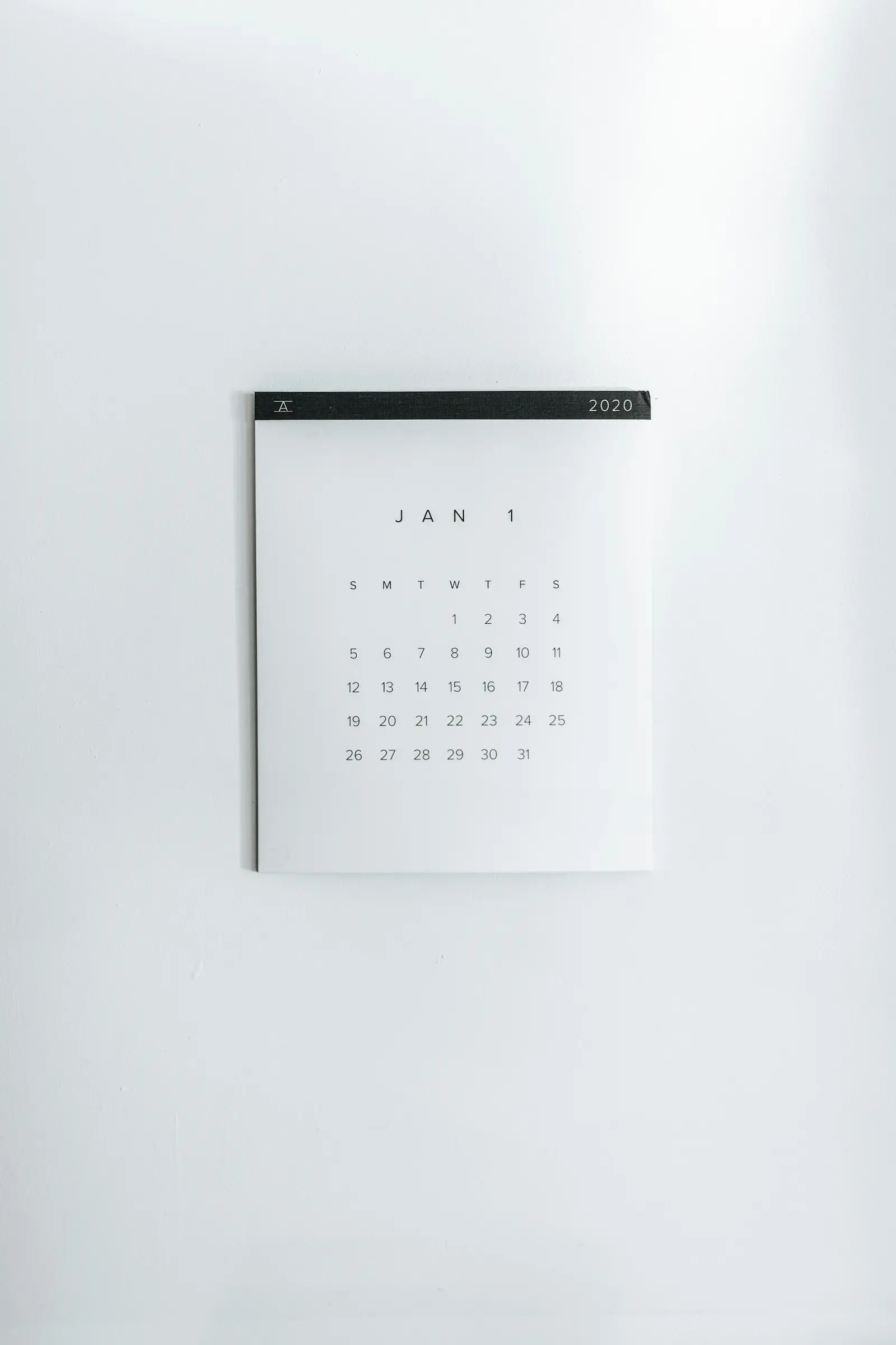 A white wall calendar for January hanging on a plain white wall.
