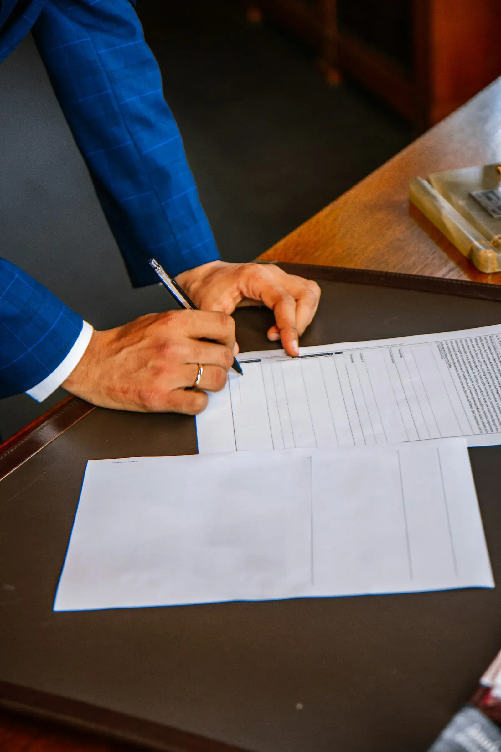 A hand holding a pen over printed forms on a desk.