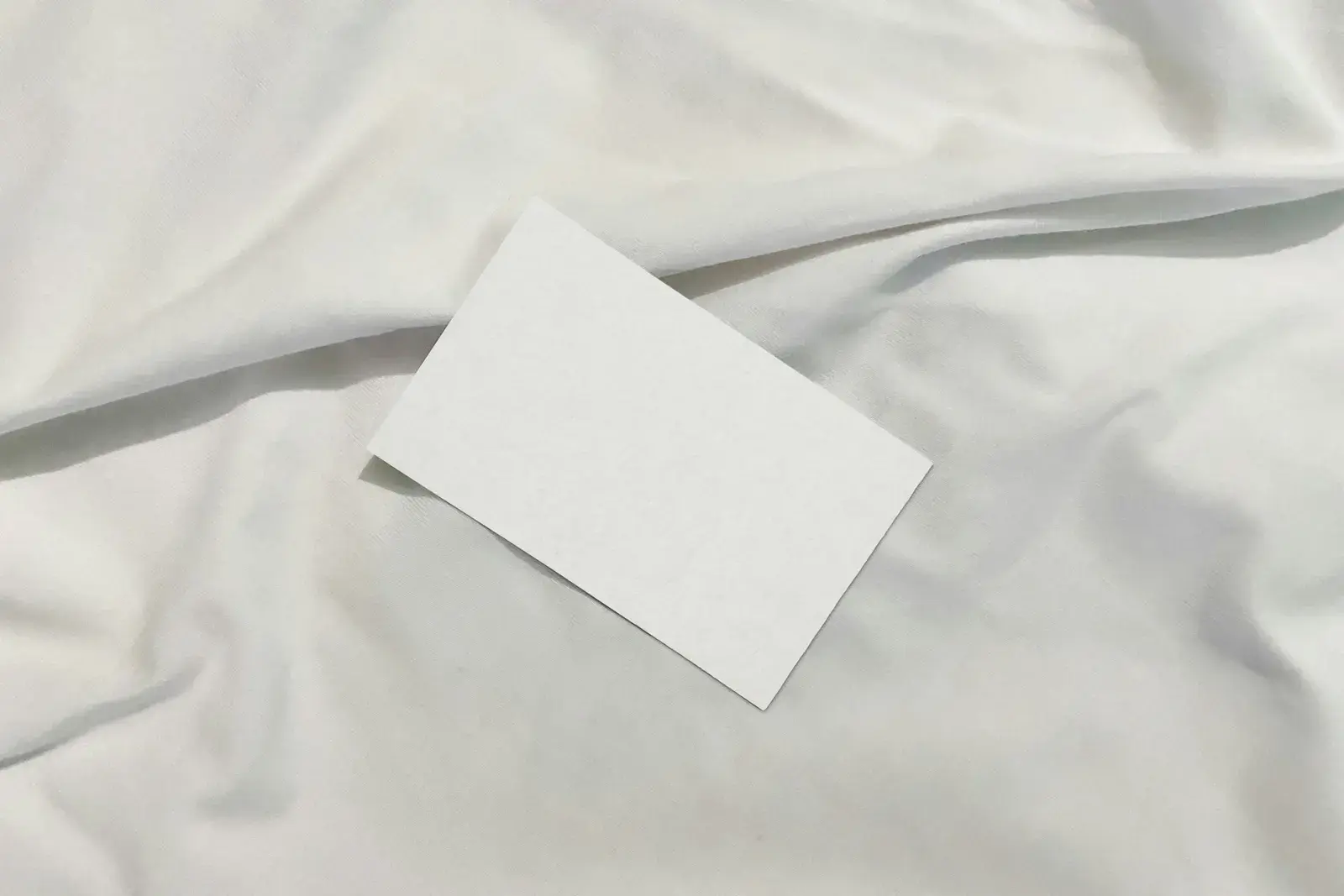 A blank white card lying on crumpled white bed linen.