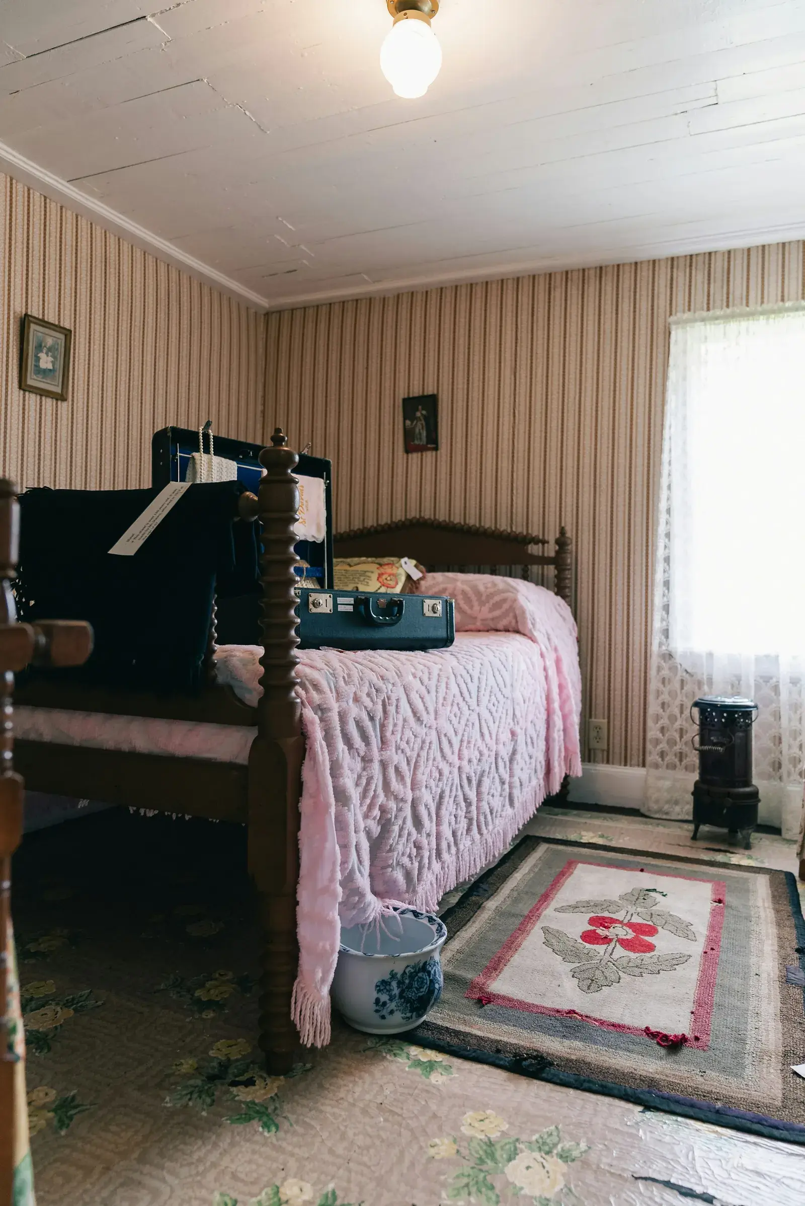 An old-fashioned bedroom with a wooden bed, a pink bedspread and a suitcase on top.