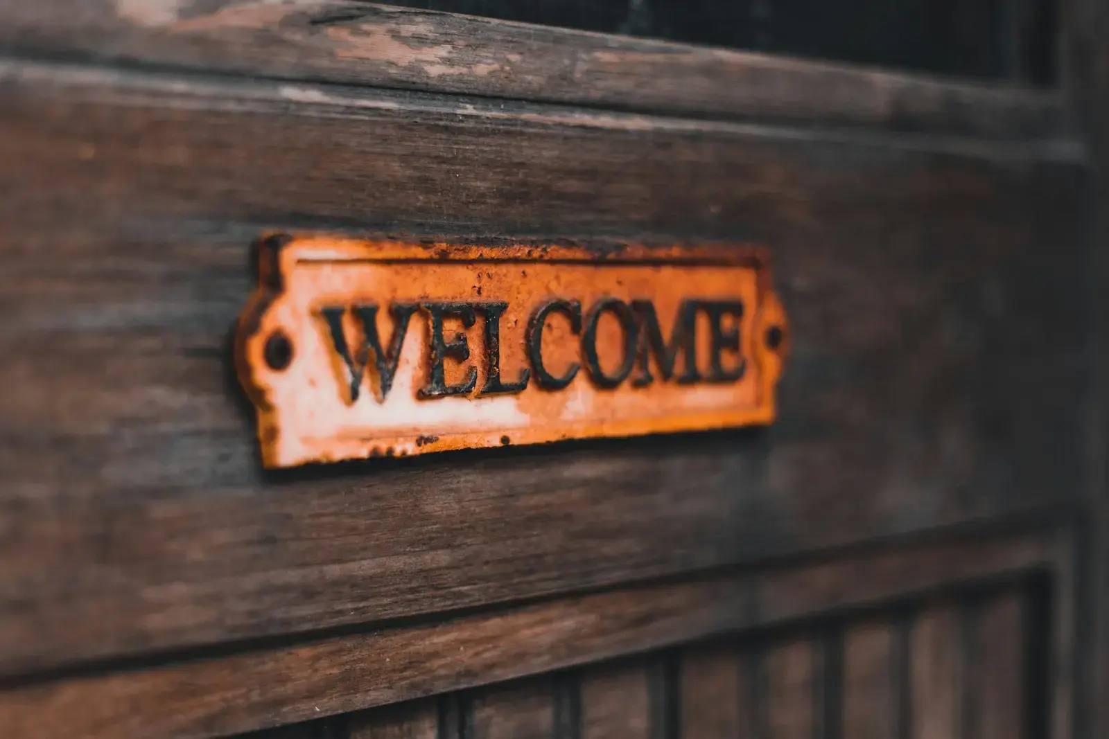 A rusty metal welcome sign mounted on a dark wooden door.