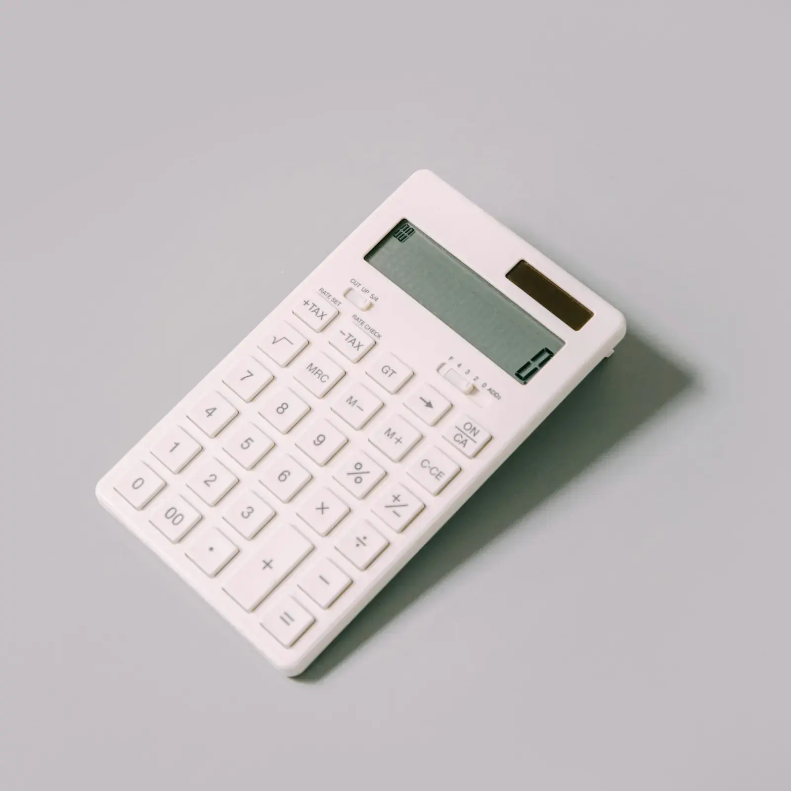 A white calculator on a light grey table.